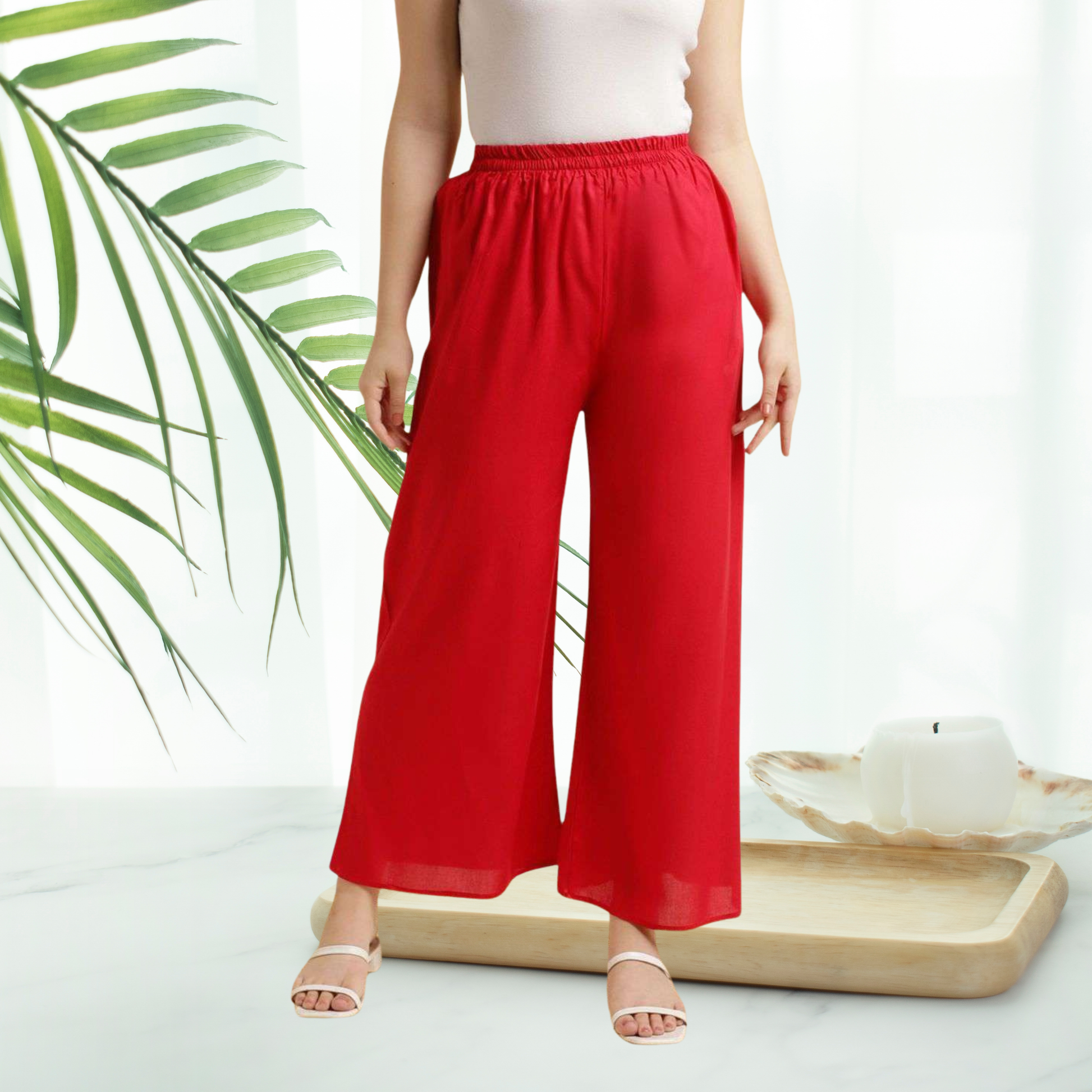 Person wearing red wide-leg pants with a white top and sandals, standing against a light background.